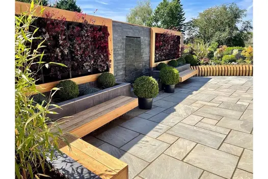 Contemporary outdoor space with Kandla Grey sandstone paving, complete with wooden benches and lush greenery.