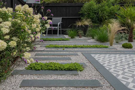 Charcoal Plank Porcelain used as stepping strips set within gravel, with geometric porcelain tiles and lush planting in a contemporary garden.