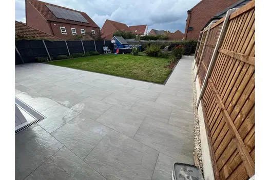 Extending seamlessly into the garden, this grey porcelain paving blends effortlessly with the well-manicured lawn and wooden fencing.