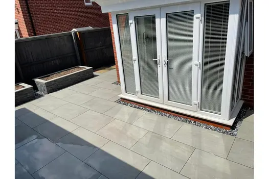 Surrounding a modern conservatory, these grey porcelain slabs are paired with gravel borders and raised planters for a refined finish.