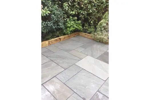 Natural Kandla Grey Sandstone patio laid in a traditional pattern, surrounded by lush planting for a timeless garden look.