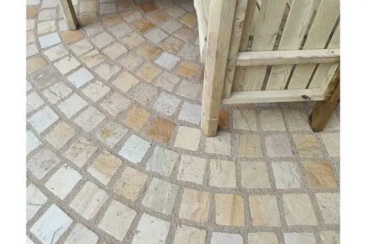 Mint Sandstone Setts laid in a curved pattern, showing the warm beige and cream tones of the stone beneath wooden garden seating.