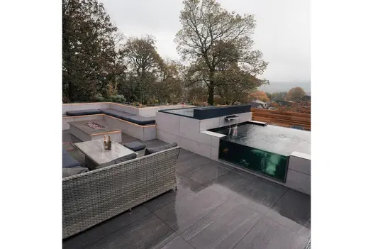 Contemporary garden lounge with Overland Dark Porcelain Paving, including a built-in koi pond and outdoor kitchen.