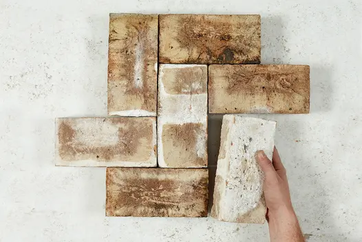 A single hand holds one brick from set of 7 London Mixture Belgian bricks laid in a small herringbone pattern against a white background.