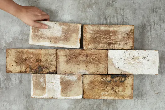Hand adds 1 brick to 6 London Mixture clay pavers laid in alternating rows of 2 and 3 bricks, showing colour variation.