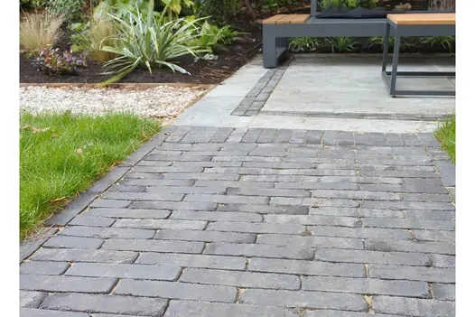 Lucca Clay Brick Pavers in a cool grey blend used as a garden pathway, bordered by grass and planting, leading toward a modern seating area with timber-topped benches.