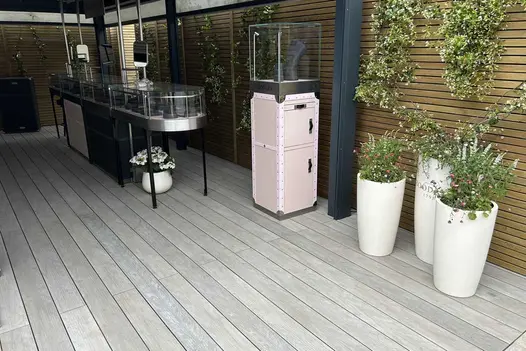 Luna DesignBoard composite decking in light grey tone forming a contemporary outdoor floor beneath a covered display area, with planters and timber slatted screening in the background.