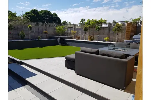 A well-designed garden space with Allora Silver Porcelain paving, lush artificial lawn, and contemporary outdoor furniture.