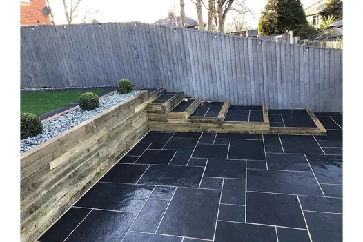A tiered garden with Midnight Black Limestone paving, wooden steps, creating a modern outdoor space with crisp, clean lines.