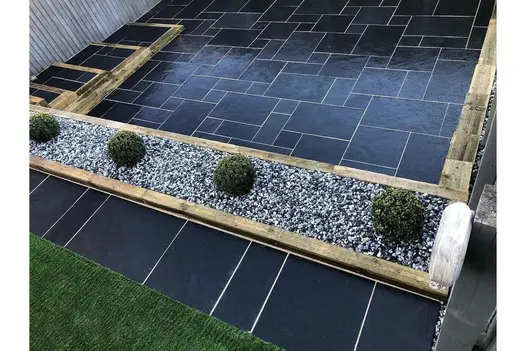 Midnight Black Limestone patio with a contemporary layout, with a gravel border and neatly trimmed shrubs.