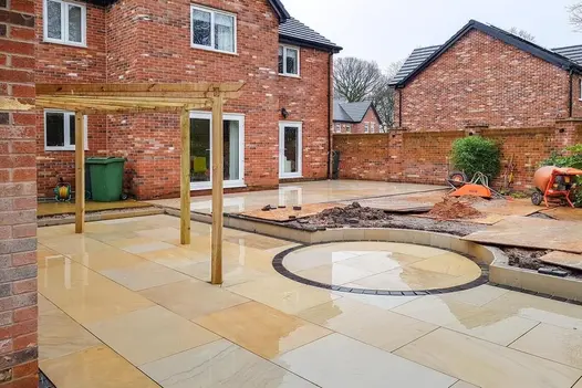 A spacious outdoor area with a Mint Smooth Sandstone patio being installed, featuring a circular design element.