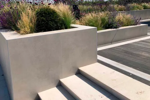Off White Porcelain Cladding used to create crisp, modern planter walls and steps, providing a clean architectural backdrop to soft grasses and purple flowering plants.