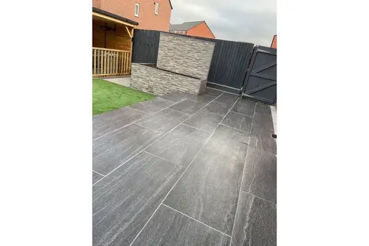 Patio paved in Overland Dark 1200x600 Porcelain paving, set against a stone feature wall and wooden fencing.