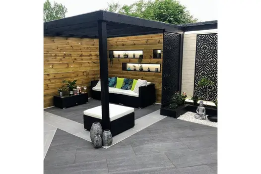 Garden seating area with Overland Dark Porcelain Paving, framed by timber fencing and black pergola.