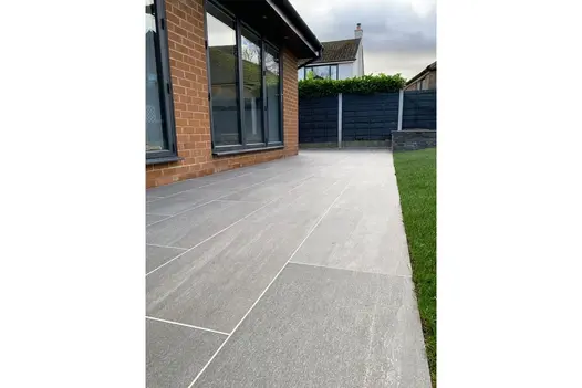 Outdoor space with Overland Dark Porcelain Paving, extending around a red-brick home and lawn edge.
