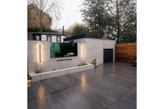 Sleek garden patio using Overland Dark Porcelain Paving, featuring a built-in koi pond and ambient wall lighting.
