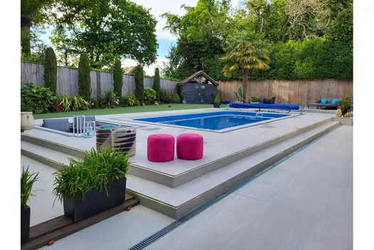 Contemporary garden with Overland Sand 1200x600 Porcelain Paving, surrounding a raised pool and vibrant seating.