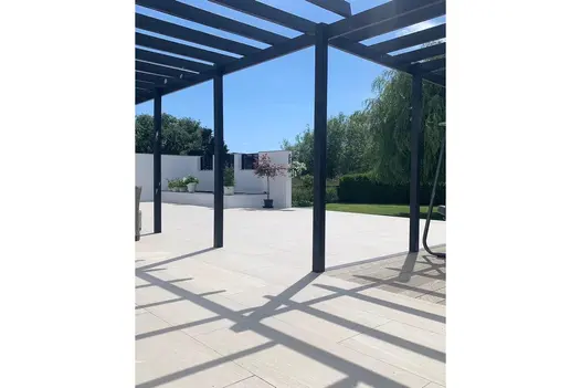Modern patio with Overland Sand paving beneath a sleek pergola, casting sharp shadows across the surface.
