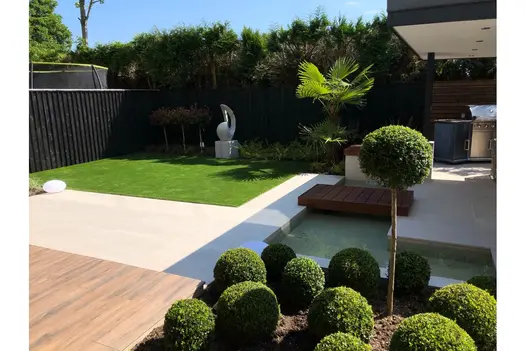 Sleek lawn bordered by Overland Sand Porcelain Paving and manicured shrubs for a modern outdoor look.