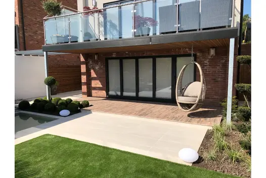 Overland Sand 900x450 Porcelain Paving laid across a rear patio, adjoining bi-fold doors and manicured lawn.