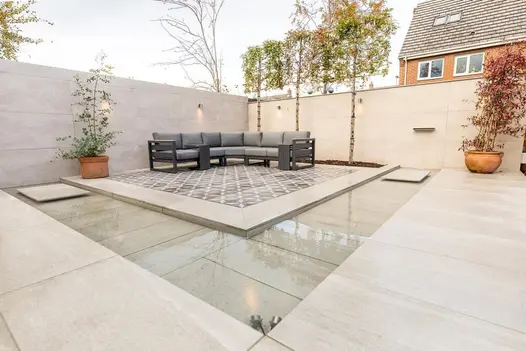 Minimalist outdoor seating area using Overland Sand Porcelain, with a shallow reflective water feature and warm-toned planters.