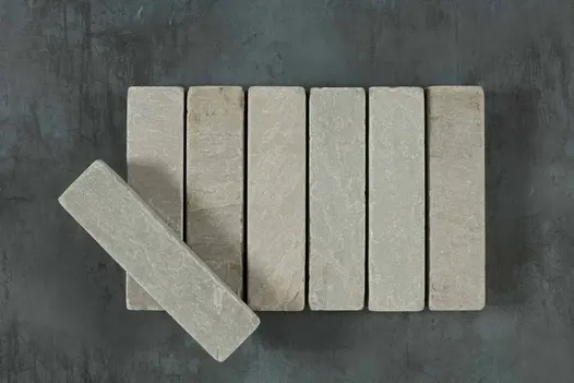 6 Kandla Grey stone pavers laid in row on grey background. A 7th brick lies at an angle on top. Free UK delivery available.