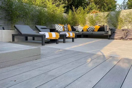 Pebble Grey Brushed Composite Decking used in a modern garden seating area with sun loungers, outdoor sofa and bamboo planting.