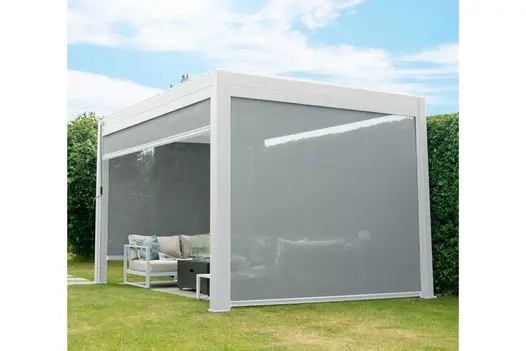 Proteus white aluminium pergola with 2 sides fully lowered shelters seating area in lawn next to hedge.