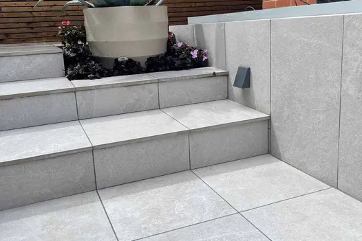 Raised patio with steps and soft landscaping, finished in 900x450 pumice porcelain paving.