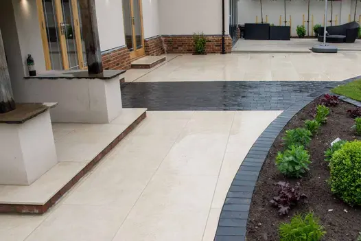 Midnight Black Limestone Setts used as a curved edging detail between the cream porcelain patio and planted borders in a contemporary garden design.