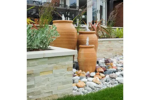 Mint Sandstone Stone Cladding applied to raised planter walls, featuring pale tones that complement terracotta water features, decorative pebbles, and lush garden planting.