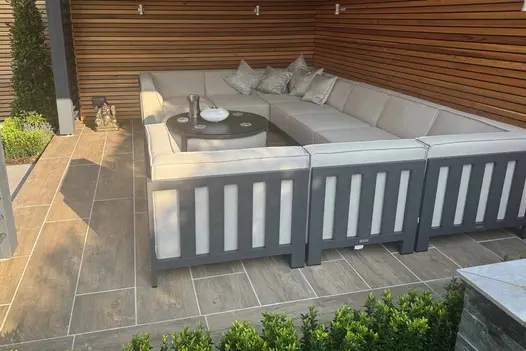 Rovere Porcelain Paving with a realistic wood-effect finish used to floor a modern outdoor seating area featuring a large corner sofa and slatted timber privacy screens.