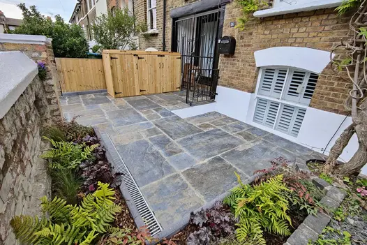 Rustic Slate Paving laid across a front garden terrace, showcasing its varied natural tones beside lush, planted borders and a traditional brick townhouse façade.