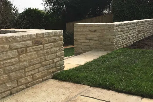 Mint Sandstone Garden Walling used to create low retaining walls, showing warm cream and beige tumbled stone blocks alongside a lawn and paved pathway.
