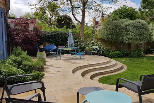 Harvest Sandstone Paving used on a curved patio with tiered steps, surrounded by mature planting and outdoor seating.