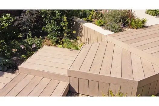 Traditional DesignBoard composite decking in a warm timber-effect finish, installed across multi-level garden platforms with angular steps beside planted borders.