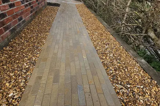 Antique Yellow Limestone Brick Pavers laid in a neat linear pattern to create a narrow garden pathway, showcasing warm golden and honey tones bordered by decorative gravel.