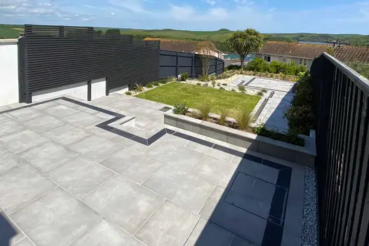 Venetian Grey Porcelain Paving used across a multi-level modern garden terrace, featuring clean lines, raised planters, and a central lawn with countryside views in the background.