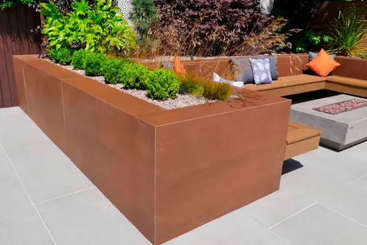 Vintage Steel Porcelain Cladding used to form a sleek, rust-toned raised planter and seating structure, adding industrial warmth and modern style to a contemporary garden lounge area.
