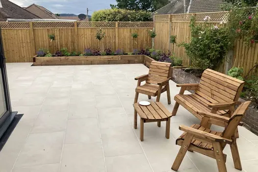 Venetian Beige Porcelain Paving used in a bright, modern garden patio with wooden outdoor furniture, raised timber planters, and a timber fence backdrop.