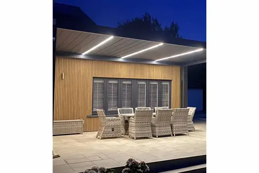 Warm Teak Composite Fence Battens installed as vertical cladding on a modern garden building, creating a warm timber finish behind an outdoor dining area under a contemporary lit pergola.