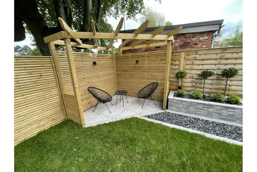 Cosy pergola corner with black chairs on light Deco 600x600 patterned tiles, framed by timber slatted fencing and raised planters.
